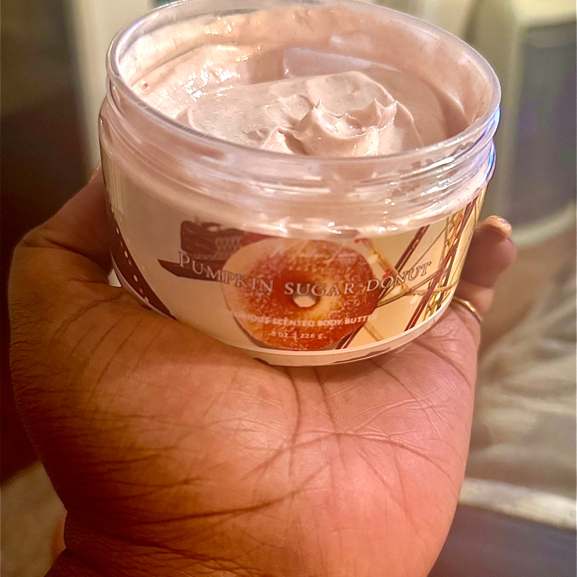 Hand holding a jar of pumpkin sugar donut scented body cream